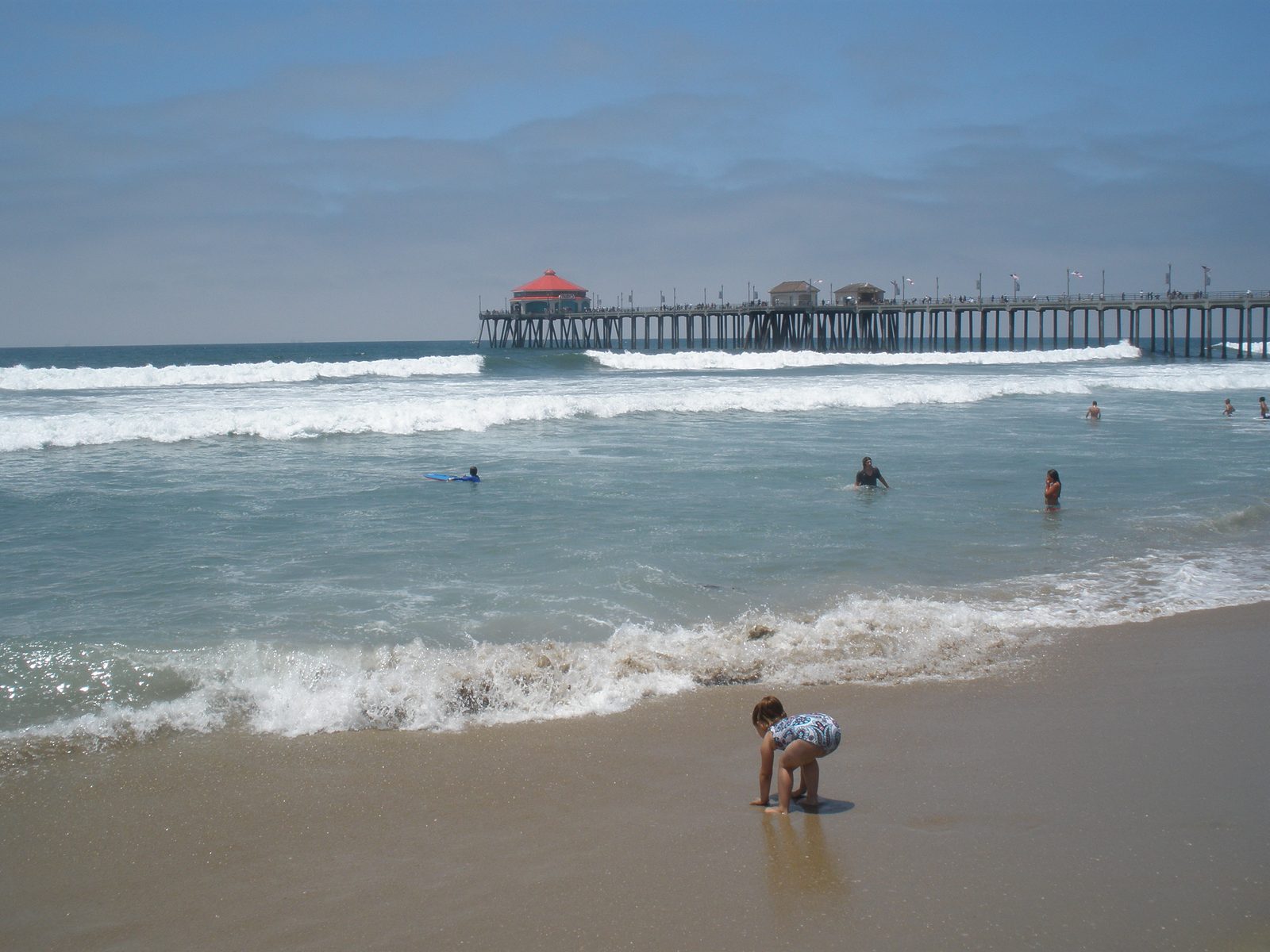 File photo: waves break in lines in front of the Huntington Beach Pier as swimmers wade in the shorebreak. The weather service expects surf of 3 to 6 feet from Sunday through Tuesday morning, with dangerous rip currents.