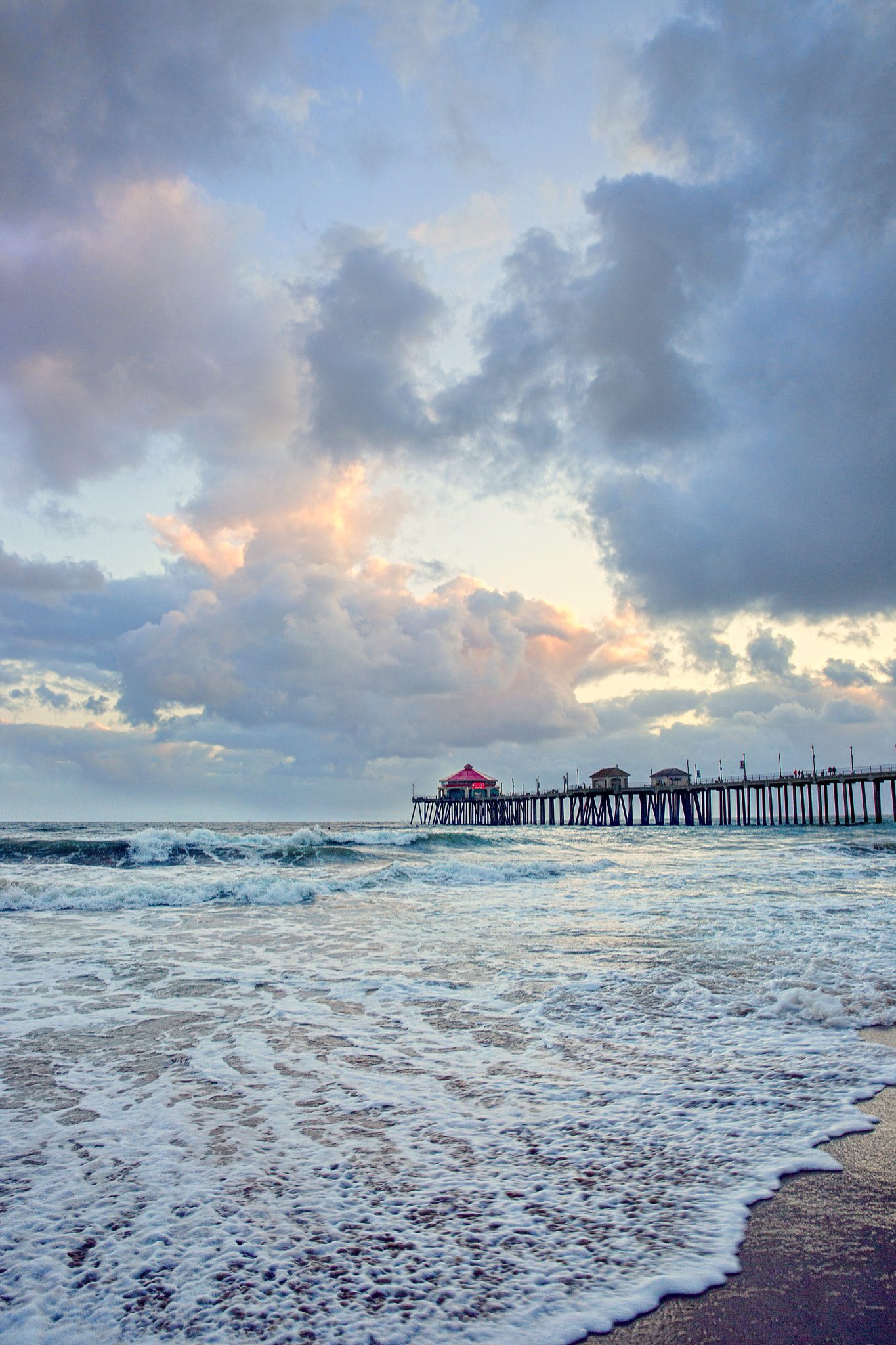 File photo: foamy surf washes onto the sand under storm clouds at the Huntington Beach Pier. The weather service said minor beach erosion may occur across south-facing beaches while the statement is in effect.